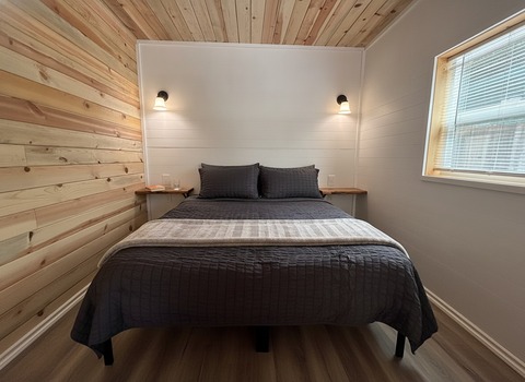 A queen bed in The Caribou at Round Mountain Retreat, made up in charcoal linen beneath two warm wall sconces on a white shiplap headboard wall.