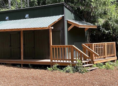 The shared bathhouse at Round Mountain Retreat from outside — a small building with a covered cedar deck and a ramp, a short walk from The Moose.
