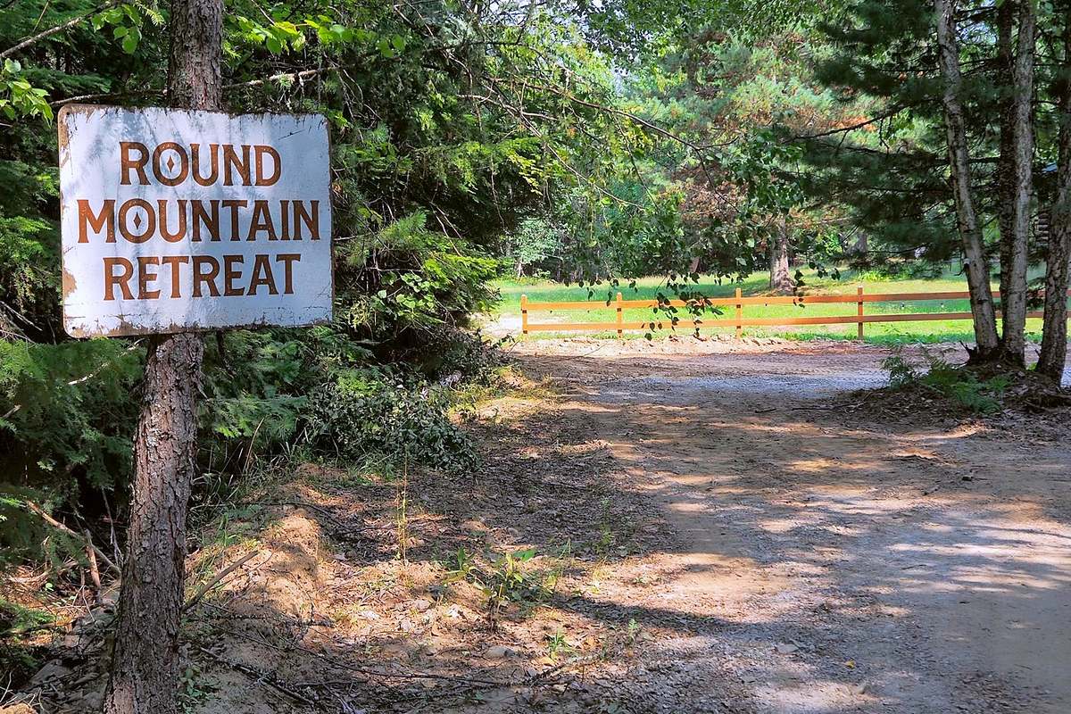The hand-painted Round Mountain Retreat sign at the entrance off Round Mountain Road, in warm summer light