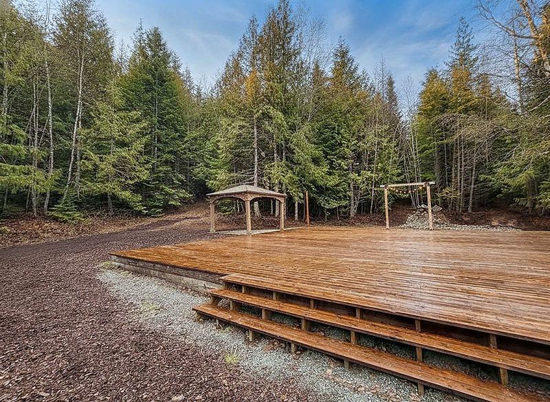 The large open-air timber deck at Round Mountain Retreat with its gazebo and string-lit arbour, backed by dense evergreen forest.
