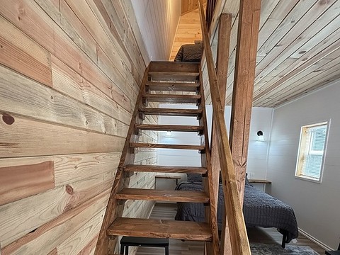 The timber loft stair inside The Caribou at Round Mountain Retreat, running up the cedar plank wall to the twin beds under the curved ceiling.
