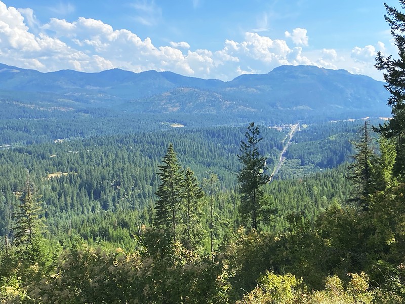 The valley view from the ridge trail above Round Mountain Retreat — forested mountains and cumulus clouds stretching to the horizon.