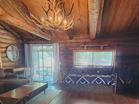 The living room inside The Elk at Round Mountain Retreat — an antler chandelier under the tongue-and-groove ceiling, a daybed beneath the window, sofa and coffee table, and a slider out to the deck.